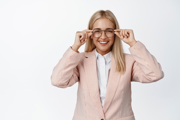 Mujer de negocios segura de sí misma con gafas mirando a la cámara con cara lista y segura de sí misma de pie en traje contra fondo blanco