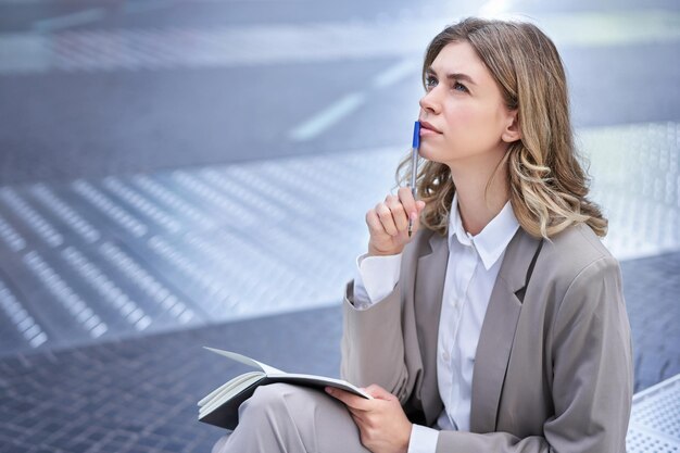 Foto gratuita mujer de negocios sentada en el centro de la ciudad con cuaderno y bolígrafo mujer corporativa escribiendo ideas thinki