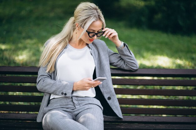 Mujer de negocios sentado en el banco en el parque hablando por teléfono
