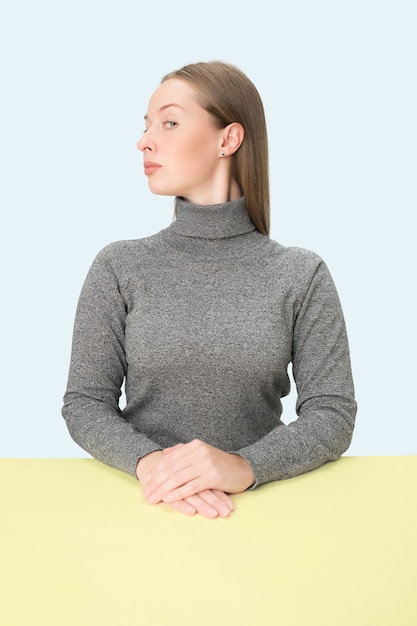 Mujer de negocios seria sentada a la mesa en un estudio rosa.