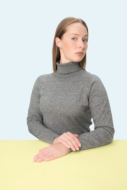 Mujer de negocios seria sentada a la mesa sobre un fondo rosa de estudio. El retrato en estilo minimalista