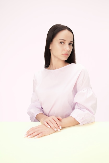 Mujer de negocios seria sentada a la mesa sobre un fondo rosa de estudio. El retrato en estilo minimalista