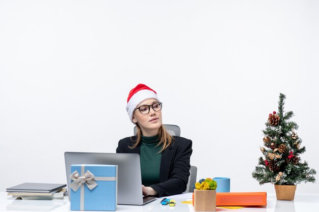 Mujer de negocios con un sombrero de santa claus sentado en una mesa con un árbol de Navidad y un regalo