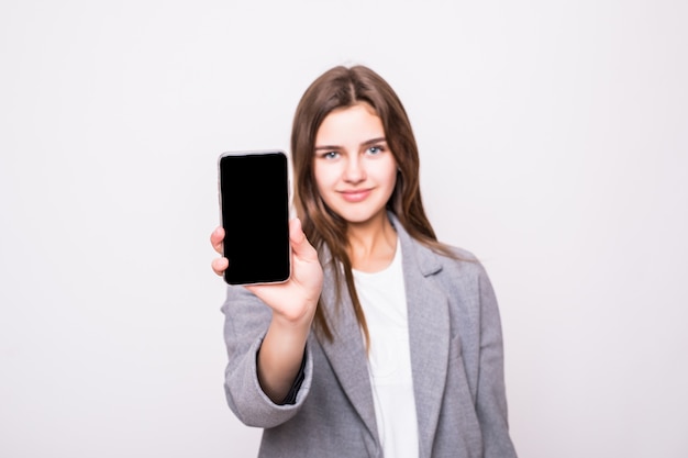 Mujer de negocios sonriendo mostrando una pantalla de teléfono inteligente en blanco sobre un fondo blanco