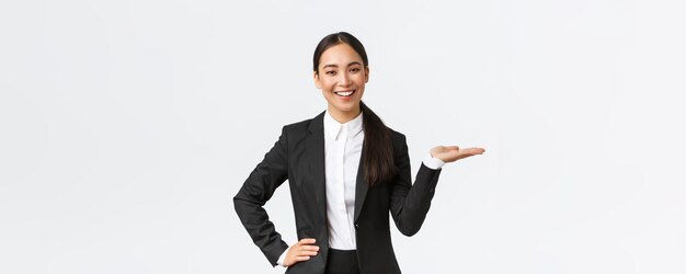 Una mujer de negocios sonriente profesional presenta su proyecto durante una reunión con una vendedora de traje negro sosteniendo la mano a la derecha mientras muestra el producto sosteniendo la palma sobre un fondo blanco en blanco