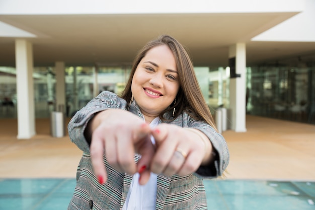 Foto gratuita mujer de negocios sonriente que señala los dedos en la cámara al aire libre