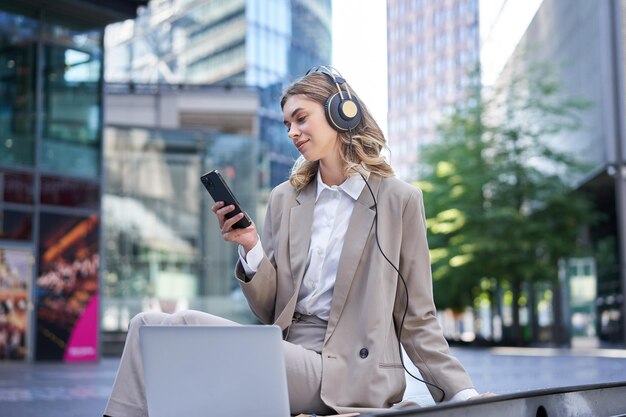 Mujer de negocios sonriente con traje sentada en una reunión en línea desde una laptop usando auriculares mirando