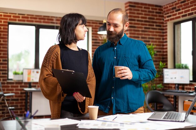 Mujer de negocios sosteniendo un portapapeles con un informe financiero que explica la estrategia de la empresa al hombre gerente con una lluvia de ideas para el proyecto de marketing. Empresarios analizando documentos en la oficina de inicio