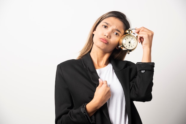 Mujer de negocios sosteniendo un reloj de alarma en la pared blanca.