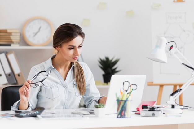 Mujer de negocios sosteniendo sus gafas y trabajando en la computadora portátil