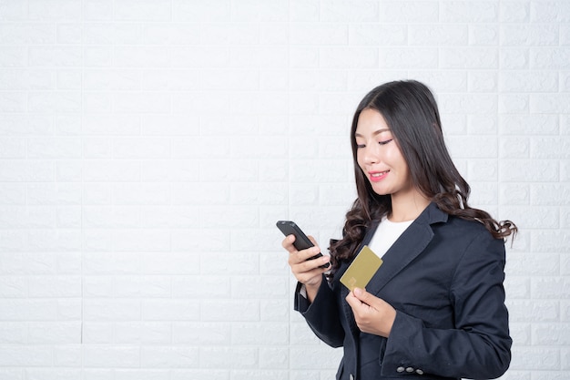 Mujer de negocios sosteniendo una tarjeta de débito separada, pared de ladrillo blanco Hizo gestos con lenguaje de señas.