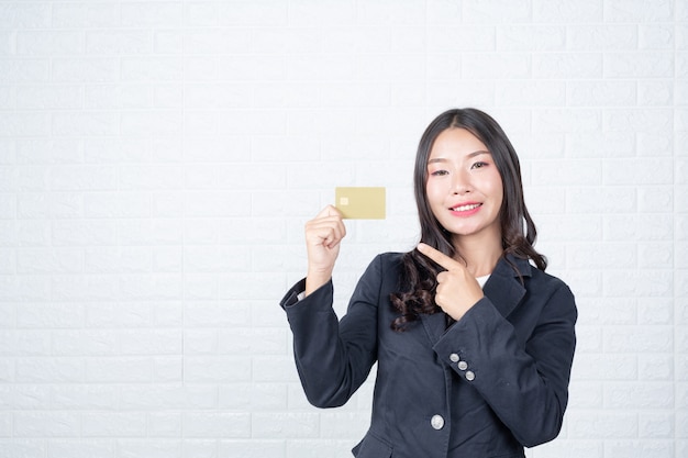 Mujer de negocios sosteniendo una tarjeta de débito separada, pared de ladrillo blanco Hizo gestos con lenguaje de señas.