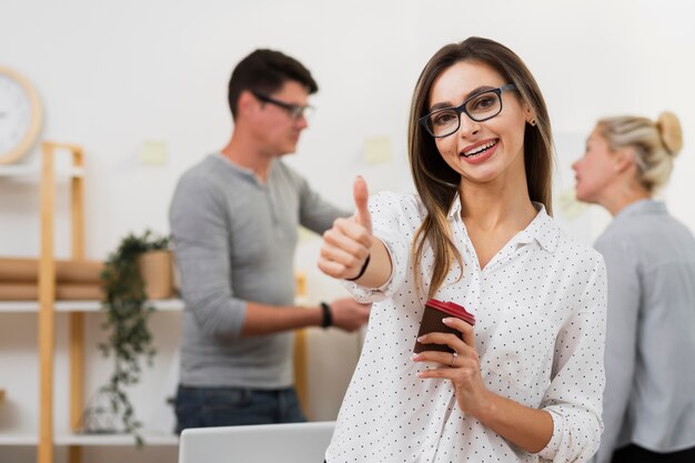 Mujer de negocios sosteniendo una taza de café y mostrando signo ok