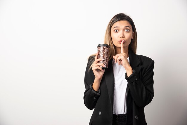 Mujer de negocios sosteniendo la taza y posando en la pared blanca.