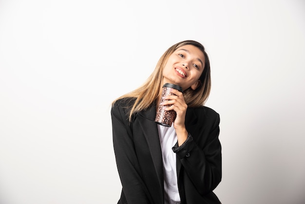 Mujer de negocios sosteniendo la taza y posando en la pared blanca.