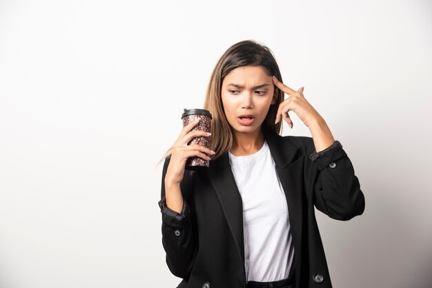 Mujer de negocios sosteniendo la taza y posando en la pared blanca.