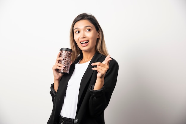 Mujer de negocios sosteniendo la taza y posando en la pared blanca.