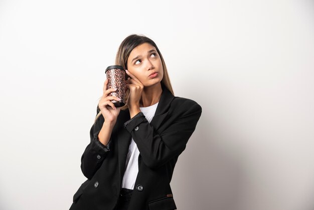 Mujer de negocios sosteniendo la taza y posando en la pared blanca.