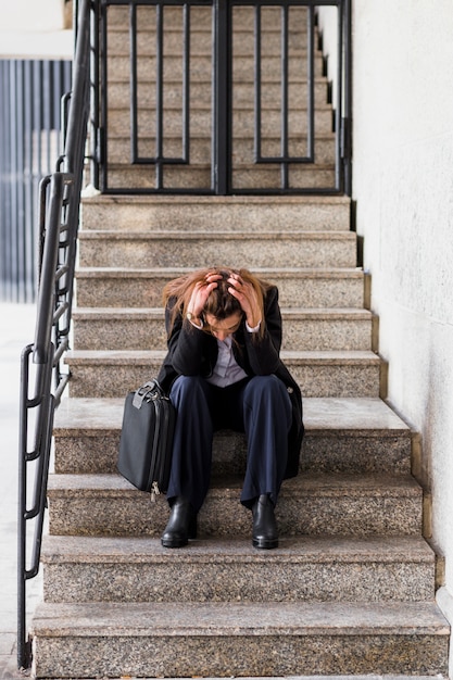 Foto gratuita mujer de negocios subrayada que se sienta en las escaleras