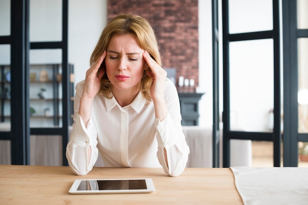 Mujer de negocios subrayada que se sienta en la tabla con la tableta