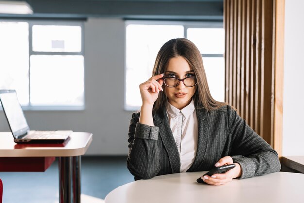 Mujer de negocios con teléfono inteligente ajustando gafas