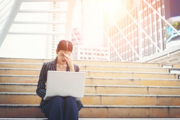 La mujer de negocios tensionado mientras que usa la computadora portátil se sienta en los pasos. Gente de negocios concepto.