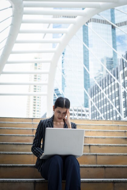 La mujer de negocios tensionado mientras que usa la computadora portátil se sienta en los pasos. Gente de negocios concepto.