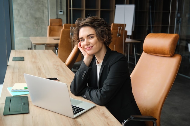 Mujer de negocios trabajando en una computadora portátil sentada en la oficina con traje esperando que el cliente prepare la documentación