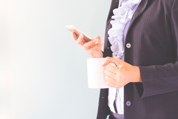 Mujer de negocios en traje oscuro celebración de teléfono móvil y una taza de café, concepto de negocio con copia espacio