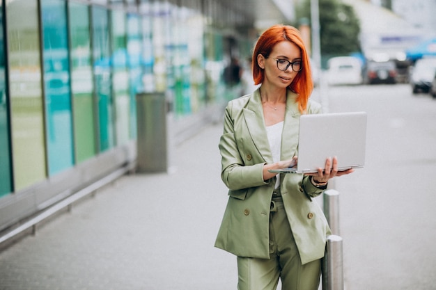 Mujer de negocios en traje verde de pie con laptop