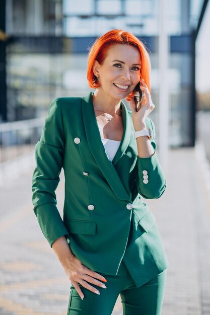 Mujer de negocios en traje verde con teléfono fuera de la calle