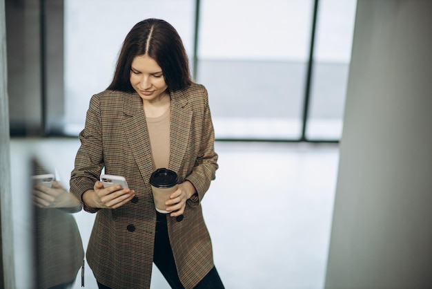 Mujer de negocios a través de teléfono móvil en el edificio de oficinas