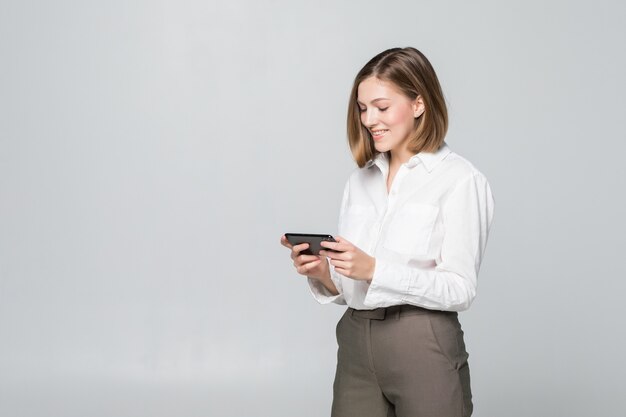 Mujer de negocios usando la aplicación en un teléfono inteligente sobre una pared blanca