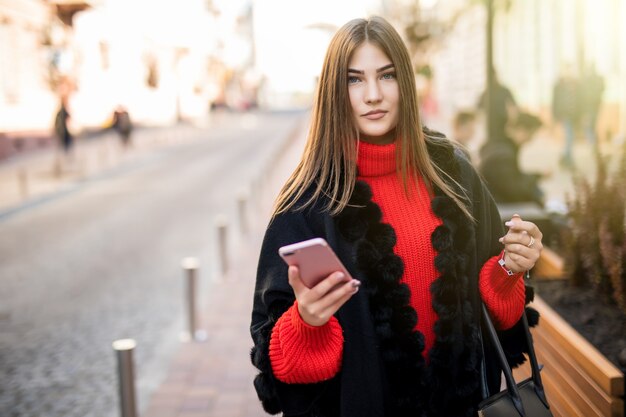Mujer de negocios utiliza teléfono inteligente en la calle mientras camina