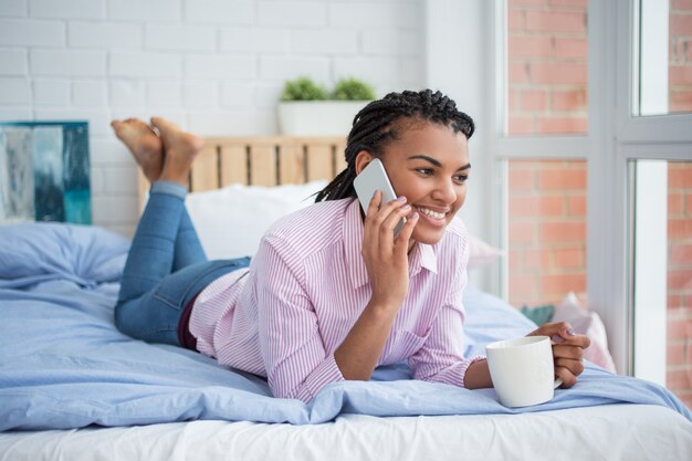 Mujer negra acostada en la cama y llamada en el teléfono