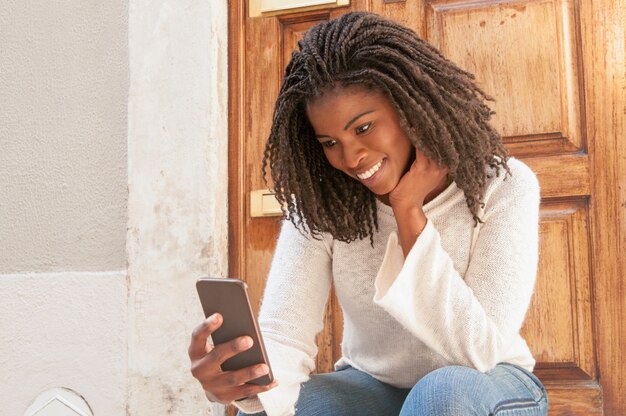 Mujer negra alegre leyendo sms encantadores de novio