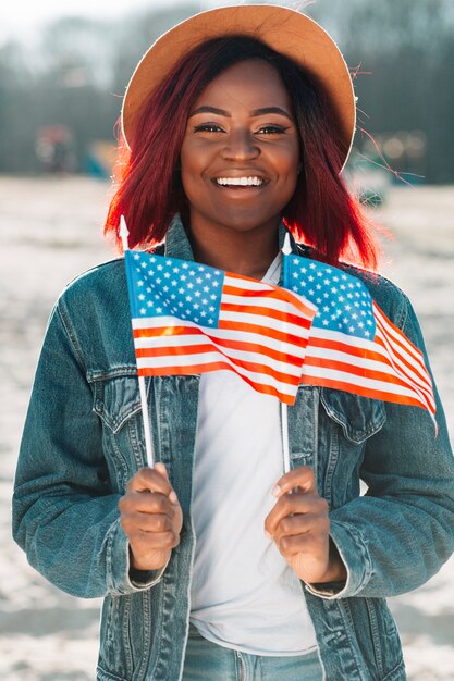 Mujer negra alegre que sostiene pequeñas banderas de los EEUU