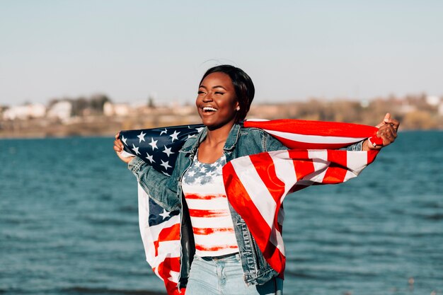 Mujer negra con bandera americana apoyada contra la espalda