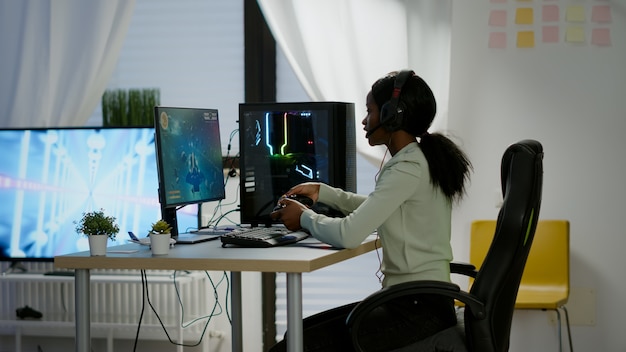 Mujer negra gamer que gana videojuegos usando un controlador inalámbrico profesional y auriculares jugando en una computadora potente. Cibernética de transmisión en línea emocionada durante un torneo de juegos usando un joystick.