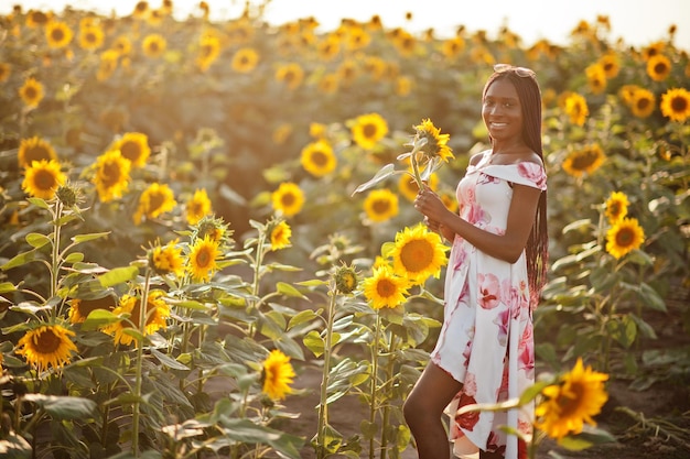 Una mujer negra muy joven usa una pose de vestido de verano en un campo de girasoles