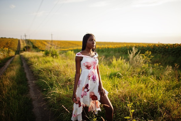 Una mujer negra muy joven usa una pose de vestido de verano en un campo de girasoles