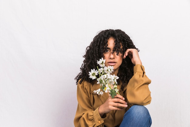 Mujer negra pensativa que sostiene las flores de la margarita