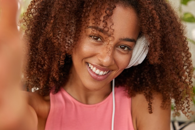 Mujer negra positiva escucha lista de reproducción favorita con auriculares