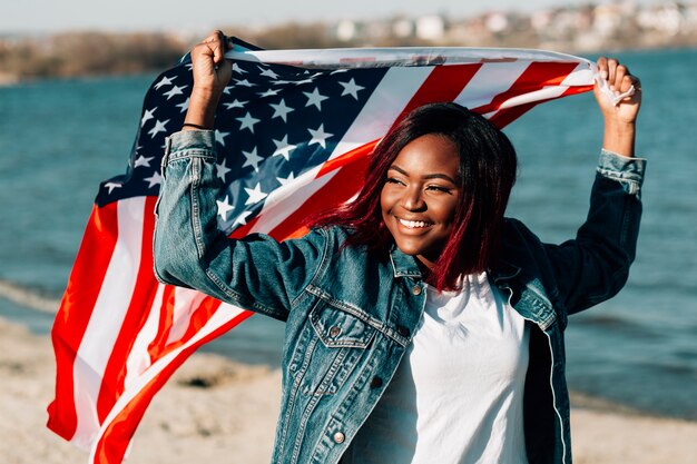 Mujer negra que sostiene la bandera estadounidense por encima de la cabeza