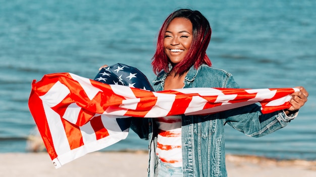 Foto gratuita mujer negra que sostiene la bandera estadounidense ondeando en el viento