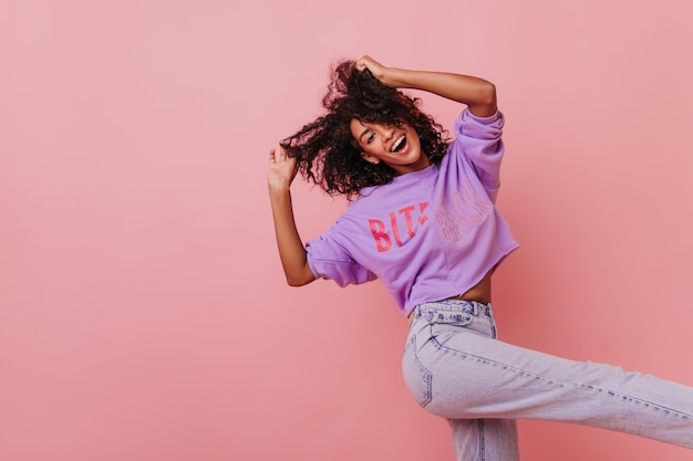 Foto gratuita mujer negra refinada en jeans blancos divirtiéndose en el estudio adorable modelo femenino rizado bailando y riendo