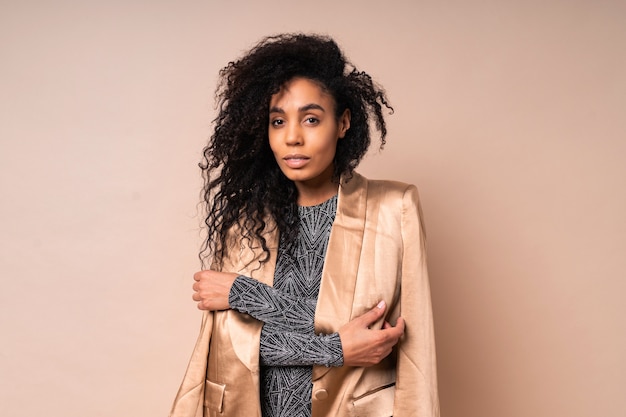 Mujer negra segura de chaqueta de seda dorada y vestido brillante con cuerpo bronceado perfecto posando.