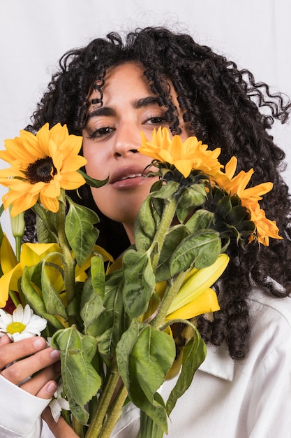 Foto gratuita mujer negra sosteniendo flores amarillas en la cara