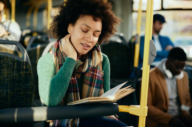 Mujer negra viajando en transporte público y leyendo un libro.