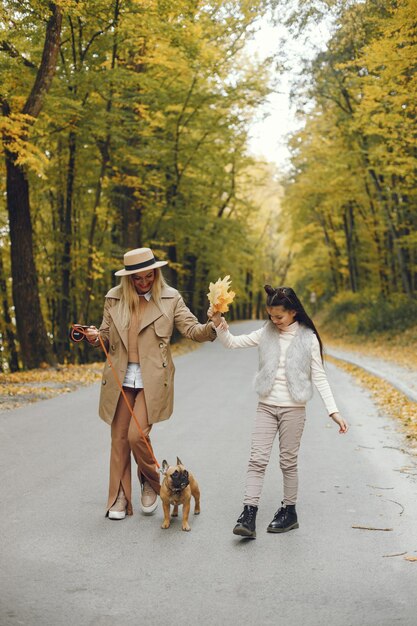 Mujer, niña y perro caminando en el parque de otoño